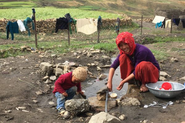 Frau mit Kind spült ihr Geschirr an einem Rinnsal im Dort Demul (Spiti)