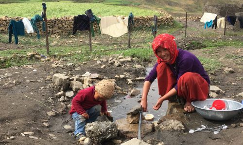 Frau mit Kind spült ihr Geschirr an einem Rinnsal im Dort Demul (Spiti)