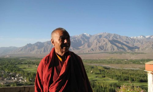 Mönch in Ladakh, im Hintergrund Felder und eine Gebirgskette