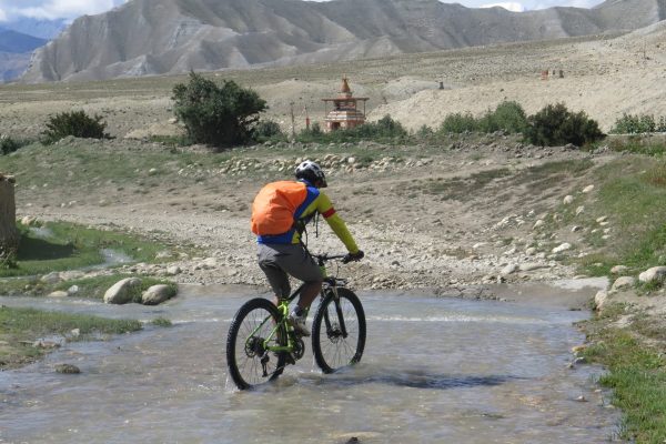 Nepal: Mountainbiker durchquert ein kleines Flüsschen.